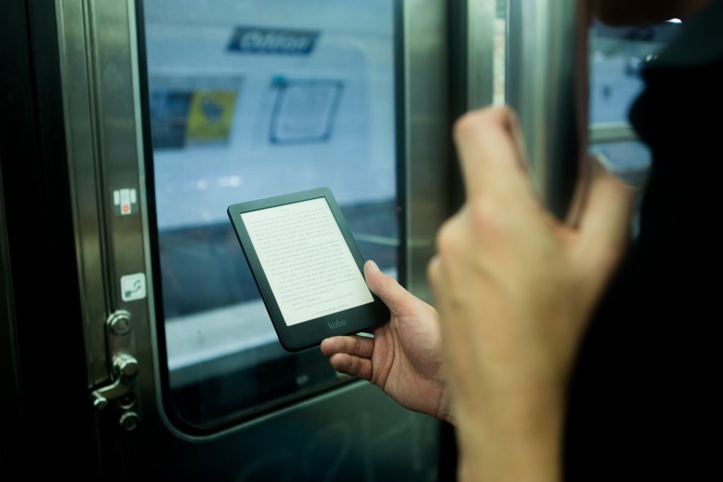 Pessoa em pé no metrô lendo um livro digital.