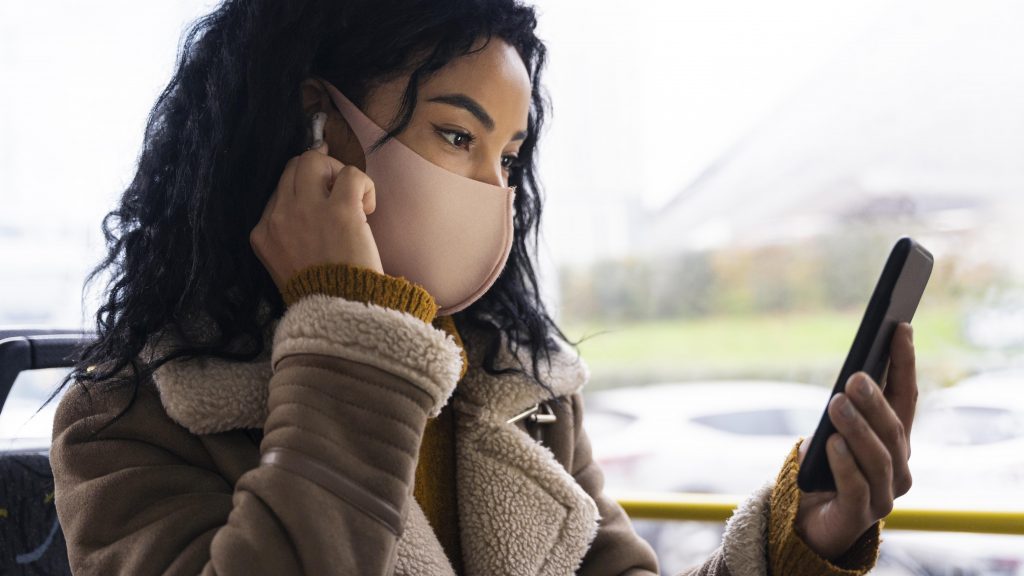 Mulher sentada no ônibus assistindo a um vídeo em seu smartphone.